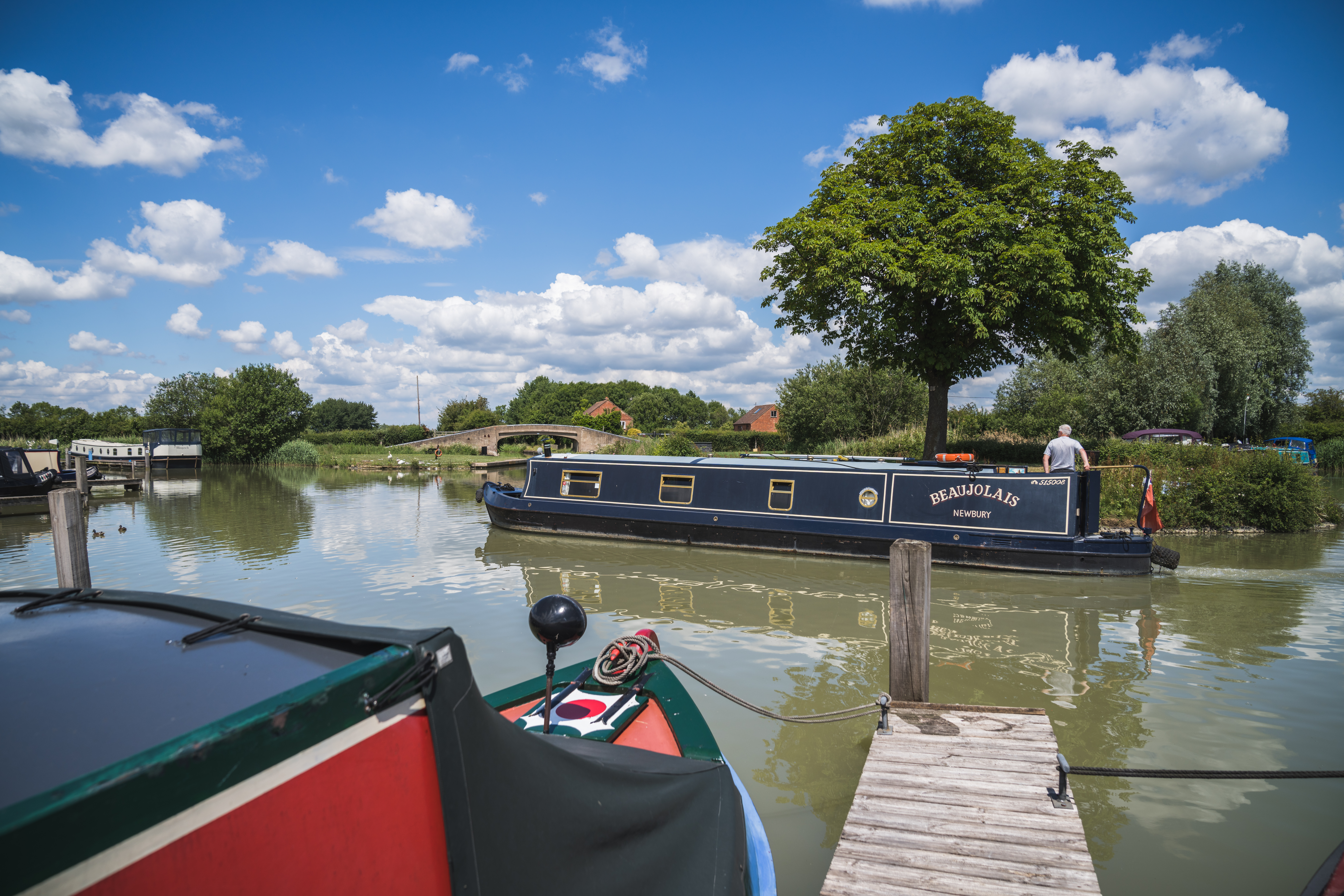 A dark blue narrowboat cruises past the jetty.
