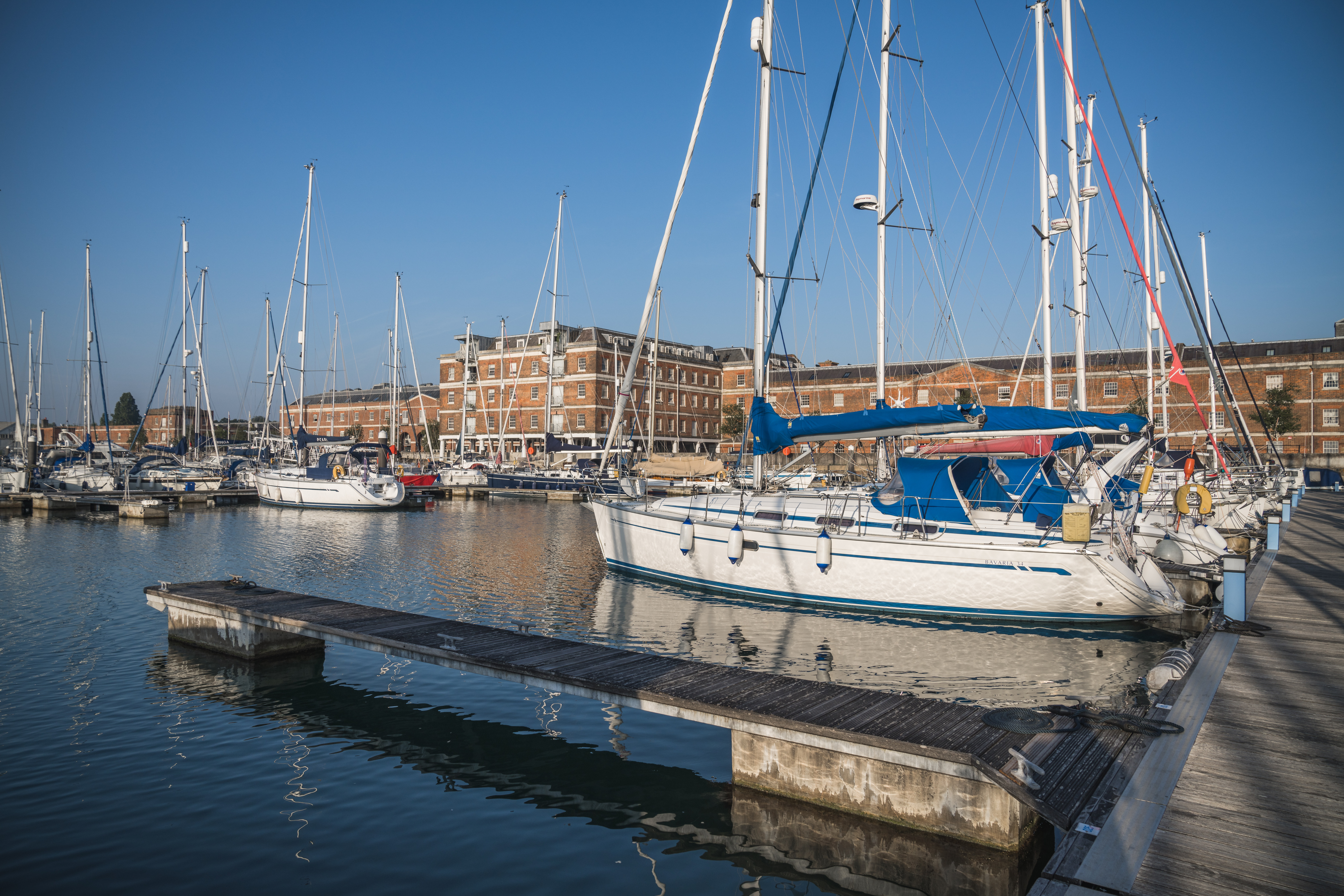 White and blue yachts sit on the water along the jetty.