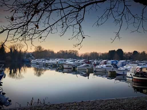 Boats at the canal side at dusk in winter, framed by trees.